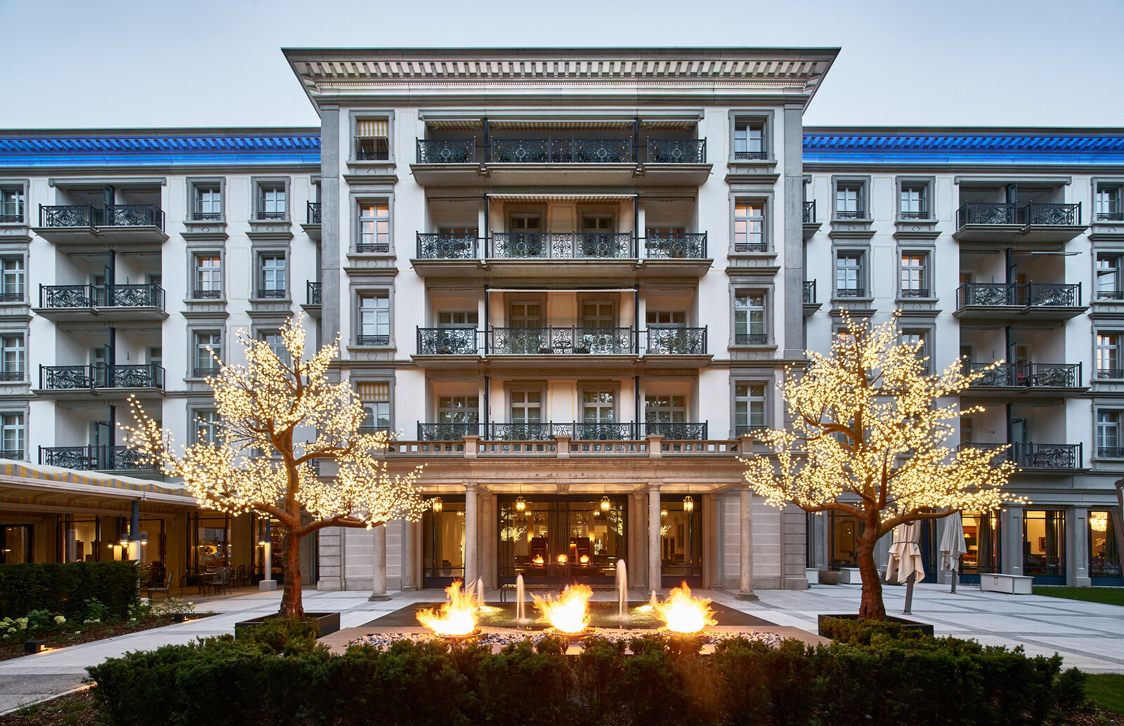 Das Hotel Quellenhof wird von vorne gezeigt. Feuer brennt auf dem Wasser und die Lichter auf den Bäumen sind eingeschaltet. Es ist ein Sterneresort in der Schweiz.