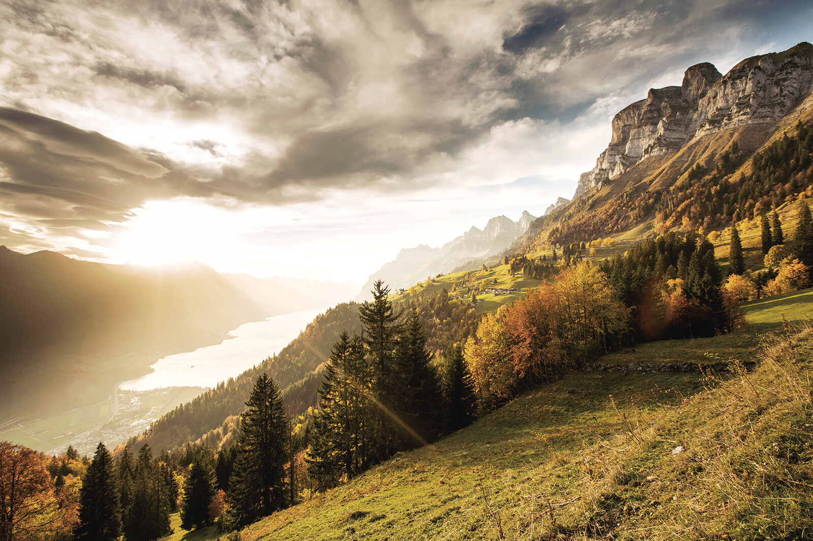 Die Sonne geht gerade hinter dem Walensee unter und erleuchtet ein letztes Mal die Landschaft des Heidilands im Herbst.