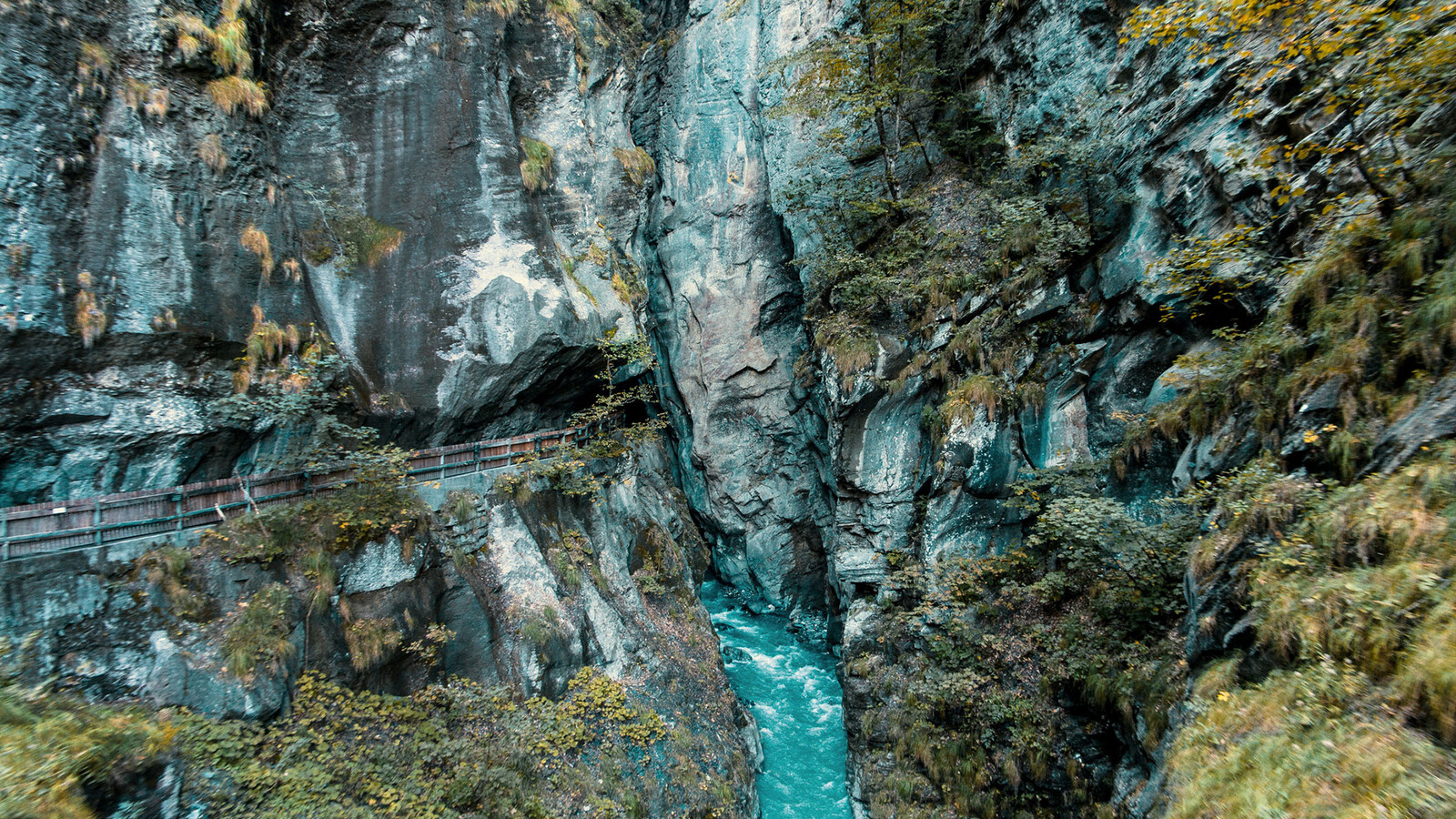 Der Weg ist zwischen den Felsen der Tamina Schlucht zu erkennen. Am unteren Rand des Bildes fliesst mittig das Wasser durch. Links und Rechts an den Rändern wächsen Büsche und Gras an den Felsen empor.