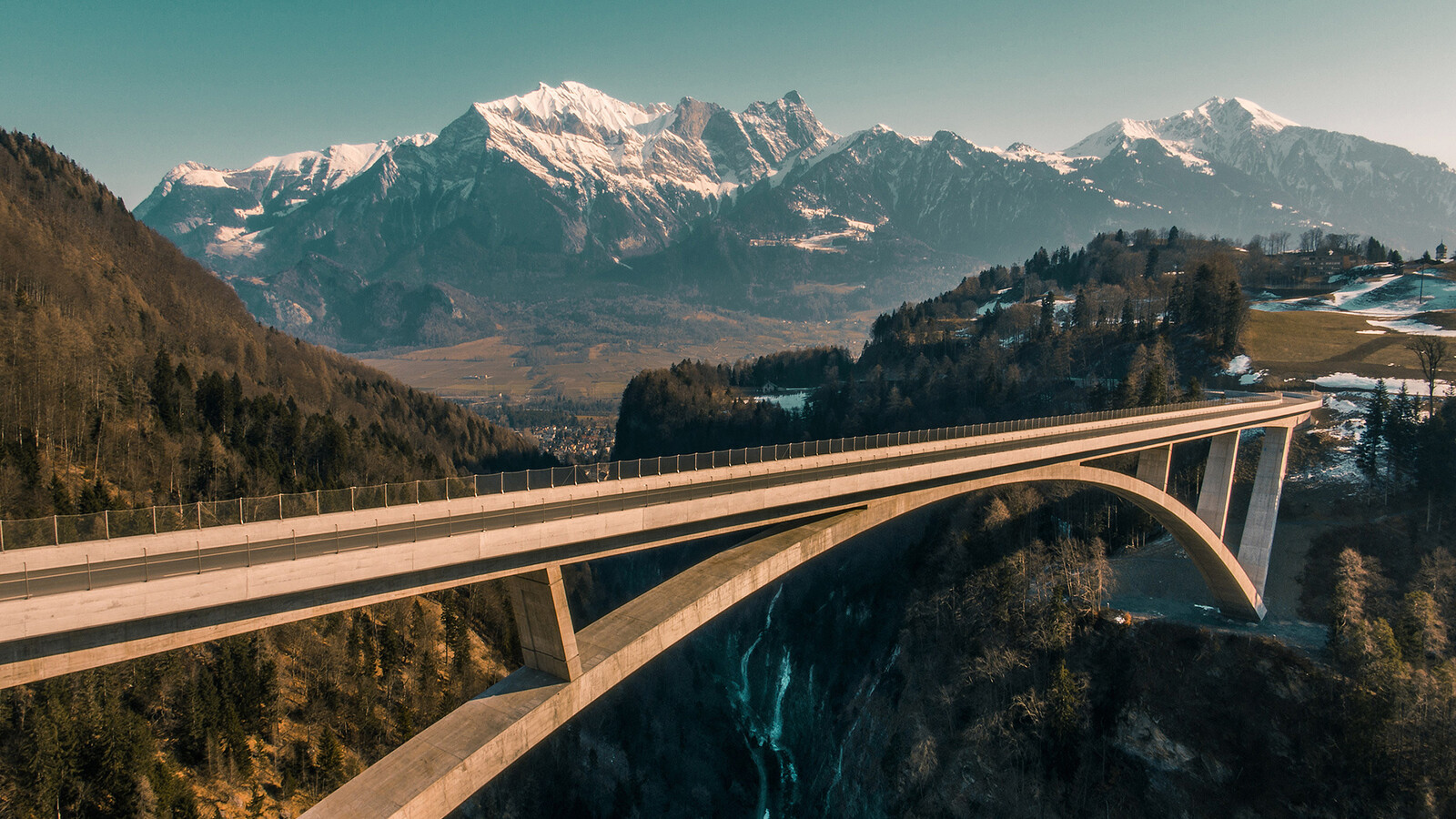 Die Taminabrücke ist in der Mitte zu sehen. Die Sonne geht unter. Berge und Wälder umzingeln die Brücke. In der Nähe befindet sich das Superior Hotel Grand Resort Bad Ragaz, ein Sternehotel in der Schweiz.